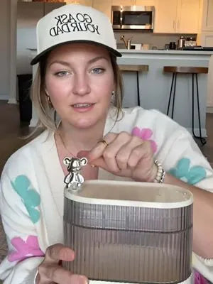 Person holding a hair tie organizer with a lid in a kitchen setting