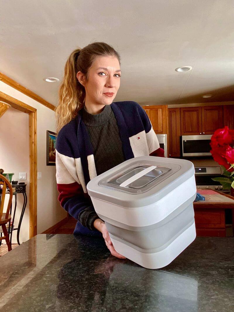 Person holding a large gray container in a kitchen